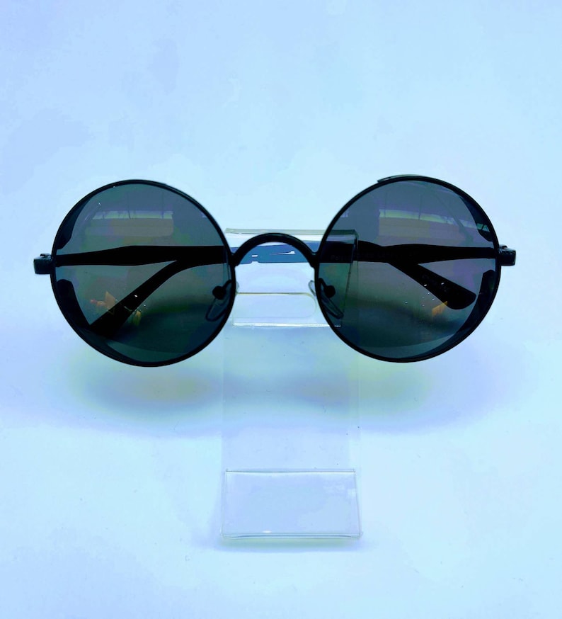 May include: Black round sunglasses with a thin metal frame. The lenses are dark and reflective.