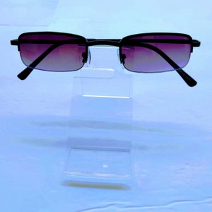 May include: A pair of black metal frame sunglasses with a gradient purple lens. The sunglasses are on a clear plastic display stand.