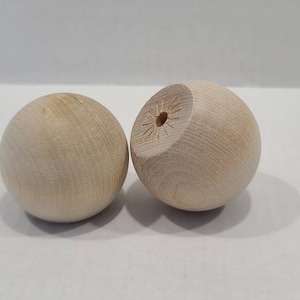 Może przedstawiać: Dwie nieoszlifowane drewniane kule, jedna z otworem wywierconym w środku.