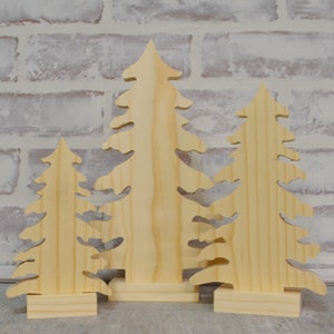 Pode incluir: Três enfeites de árvore de Natal de madeira em tamanhos diferentes. As árvores são feitas de madeira natural e têm um visual rústico. São perfeitas para adicionar um toque de alegria natalina à decoração da sua casa.