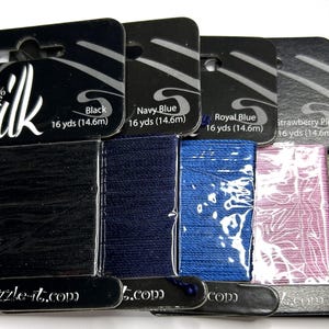 May include: Five cards of 100% pure silk thread in black, navy blue, royal blue, strawberry pink, and dark green. Each card contains 16 yards (14.6m) of thread, labeled with the color name and the Dazzle-it.com website on the black packaging.