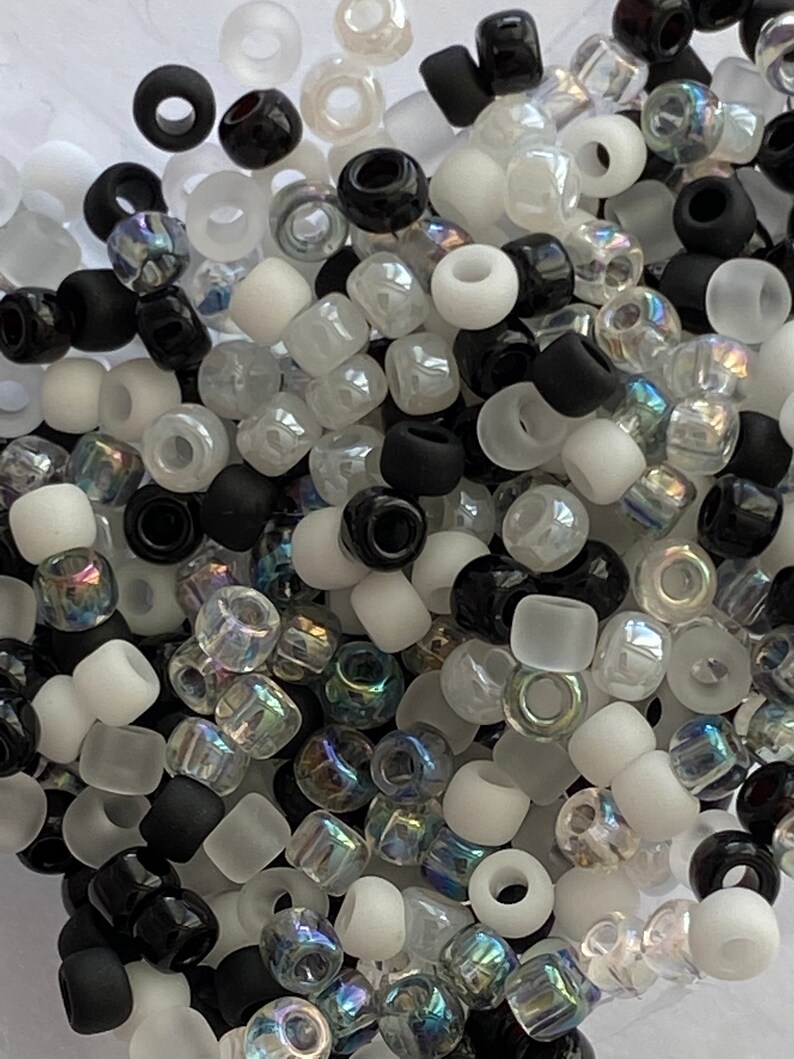 May include: A mix of black, white, and iridescent glass beads. The beads are small and round, and they are perfect for jewelry making or other craft projects.