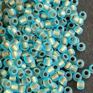 Peut inclure: Un tas de perles de rocaille en verre bleu clair avec un reflet métallique.