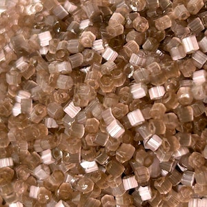 May include: A close-up shot of a collection of small, translucent, brown crystals with white interiors. The crystals are hexagonal and tightly packed, forming a textured surface. The lighting accentuates the facets of the crystals.