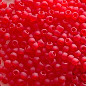 Peut inclure: Gros plan sur une grande quantité de petites perles de rocaille opaques de couleur rouge. Les perles sont rondes et ont une finition légèrement mate.