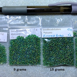 Peut inclure: Quatre sachets de perles de rocaille vertes &eacute;tiquet&eacute;s avec le nom de la marque "SeedBeadsGalore" et le poids des perles en grammes. Les sachets sont &eacute;tiquet&eacute;s avec la couleur des perles "Rainbow Emerald" et "Emerald Rnbw".
