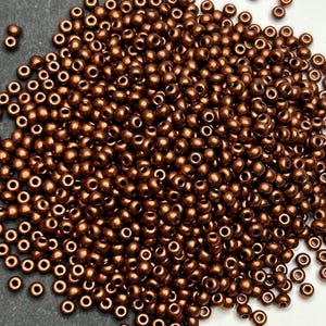Peut inclure: Un grand tas de petites perles rondes de couleur cuivre. Les perles sont toutes de la même taille et de la même forme, et elles sont disposées de manière aléatoire.