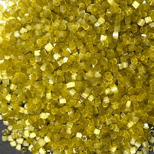 May include: A large pile of small, shiny, yellow glass beads. The beads are all the same size and shape, and they are arranged in a random pattern.
