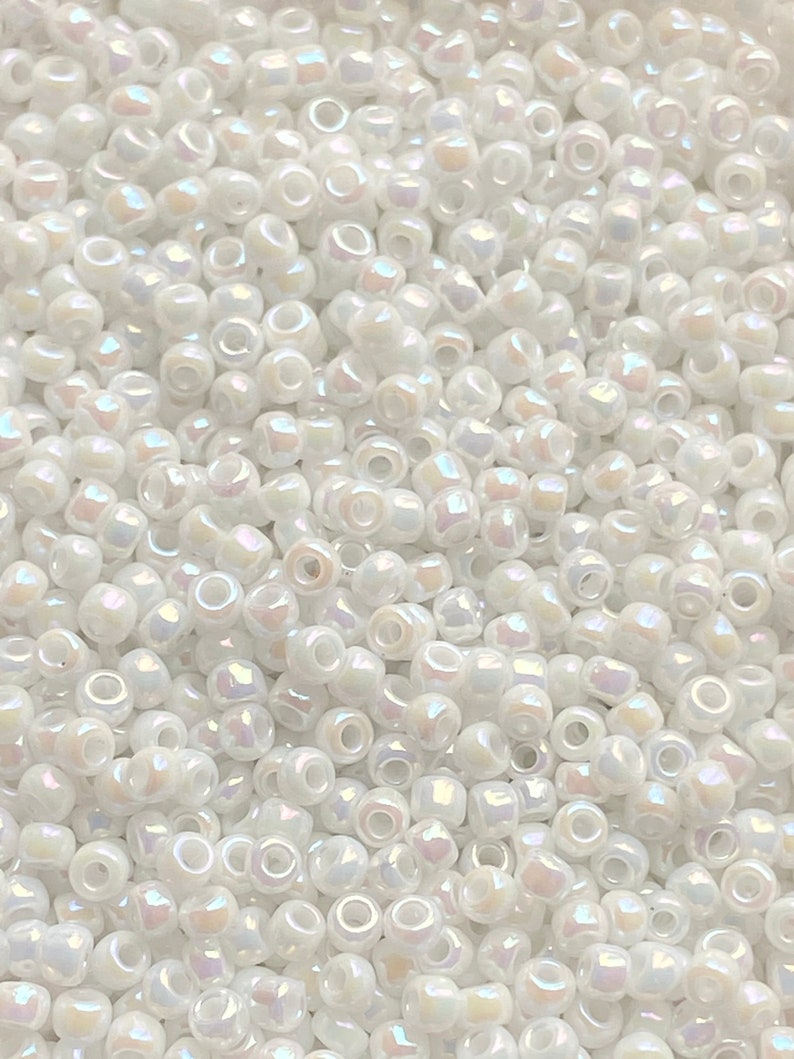 Peut inclure: Gros plan sur une grande quantit&eacute; de petites perles de rocaille blanches. Les perles ont un l&eacute;ger reflet iridescent.