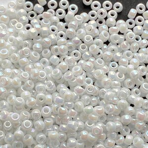 Peut inclure: Un grand nombre de petites perles de rocaille blanches et iris&eacute;es. Les perles sont rondes avec un trou au centre.