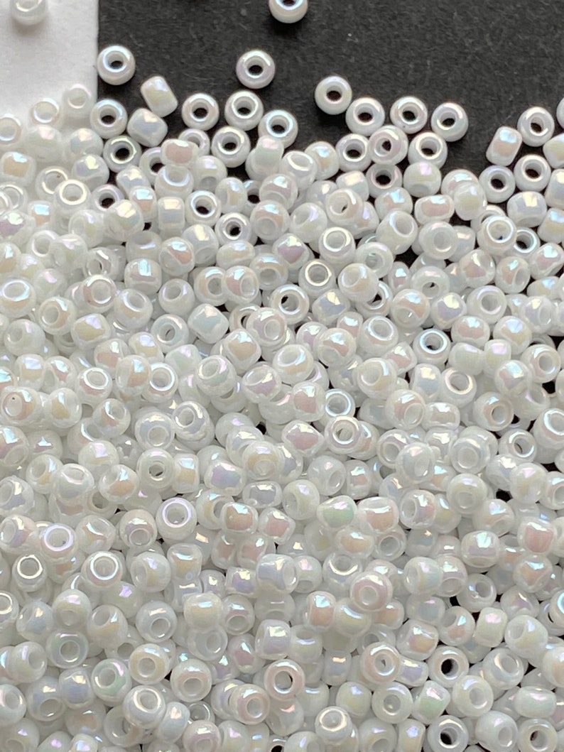 Peut inclure: Un grand nombre de petites perles de rocaille blanches et iris&eacute;es. Les perles sont rondes avec un trou au centre.