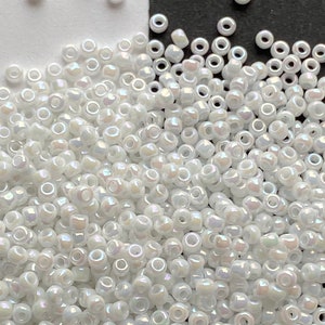 Peut inclure: Un grand tas de perles de rocaille blanches iris&eacute;es. Les perles sont petites et rondes, avec un l&eacute;ger &eacute;clat.