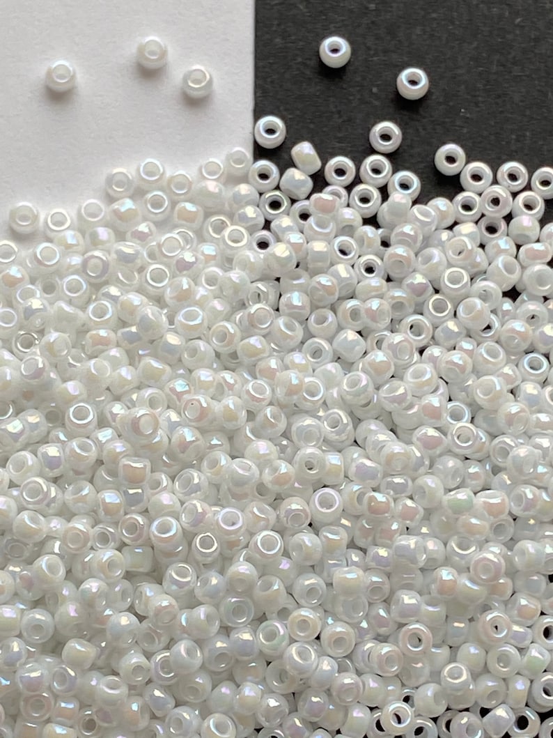 Peut inclure: Un grand tas de perles de rocaille blanches iris&eacute;es. Les perles sont petites et rondes, avec un l&eacute;ger &eacute;clat.