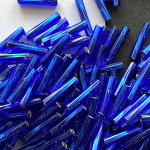 May include: A large pile of blue glass beads, each bead is a long cylinder with a reflective finish.