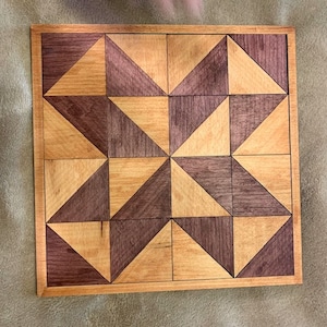 May include: A square wooden board with a geometric pattern made of light and dark wood. The pattern is made up of triangles that are arranged in a repeating pattern.