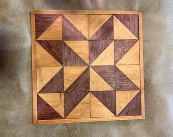May include: A square wooden board with a geometric pattern made of light and dark wood. The pattern is made up of triangles that are arranged in a repeating pattern.