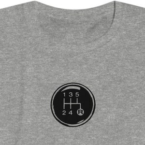 以下が含まれることがあります： 車のシフトパターンを黒と白で描いたグレーのTシャツ。数字の1、3、5と、文字のR、2、4が見える。