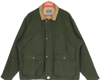 Può includere: Una giacca di lana verde scuro con colletto in velluto a coste e diverse tasche. La giacca ha un cordoncino in fondo e una chiusura con bottoni.