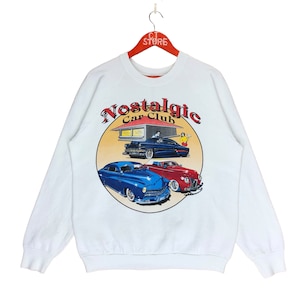 May include: White sweatshirt with a vintage car club graphic. The graphic features three cars, a red car, a blue car, and a black car. The text on the graphic reads "Nostalgic Car Club".