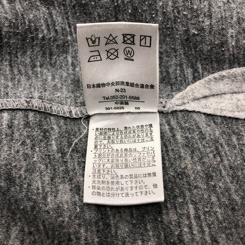 May include: A white tag with black text and symbols. The tag contains washing instructions and information about the Japanese Textile Wholesalers Association. The text reads "N-23", "Tel.052-201-5588", "China", "391-5825", "05".