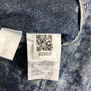 Op de afbeelding: Een wit label met een QR-code en tekst in het Japans. Het label is bevestigd aan een blauw denim jack met een wit splatterpatroon.