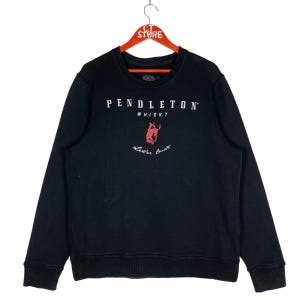 May include: Black crew neck sweatshirt with the text "PENDLETON WHISKY" in white. Below the text is a red graphic of a bucking bronco and the words "Let'er Buck" in cursive.