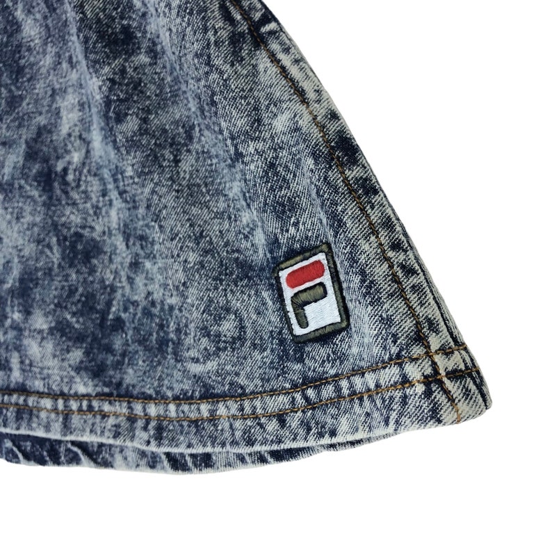 Op de afbeelding: Een blauwe denim rok met een wit en rood Fila logo patch.