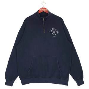 Könnte beinhalten: Ein marineblauer Quarter-Zip-Sweatshirt mit einer Kängurutasche und einem gestickten Ankerlogo mit der Aufschrift "Cape Cod Est. 1982".