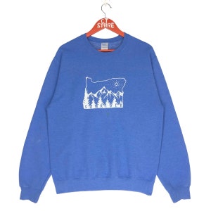 May include: A blue sweatshirt with a white graphic of a mountain range and the text "Sunriver" on the front.