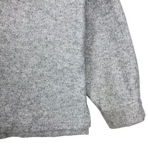 May include: A gray long-sleeved shirt made of a soft, textured fabric. The shirt has a relaxed fit and a slightly longer length.