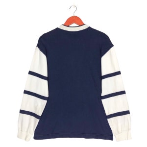 May include: A navy blue long-sleeved shirt with white striped sleeves. The shirt has a collared neckline and a button closure.