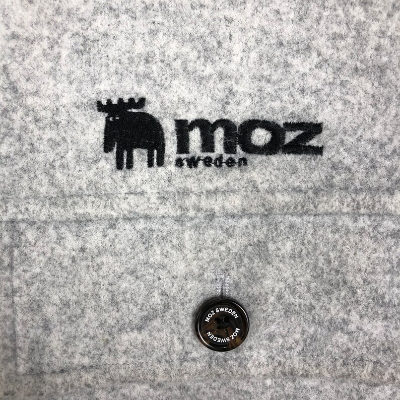 May include: A gray felt fabric with a black embroidered moose and the text "moz sweden". A black button with the text "moz sweden" is also visible.