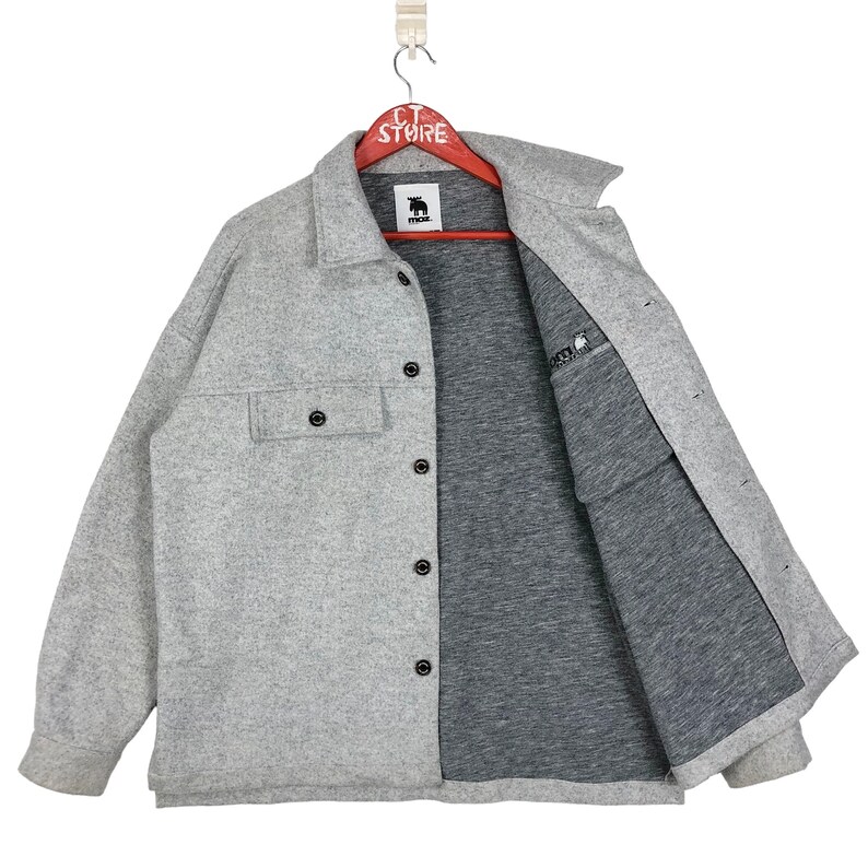 May include: A gray long-sleeved shirt with a button-up front and a single chest pocket. The shirt has a black logo on the left side of the chest that says "MUCK".