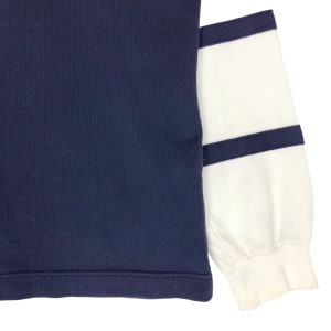 May include: A navy blue long-sleeved sweater with white ribbed sleeves and navy blue trim.