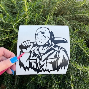Op de afbeelding: Zwart-witte vinyl sticker van een personage met een hockeymasker dat een machete vasthoudt. Het personage draagt een jas en heeft een dreigende uitdrukking.