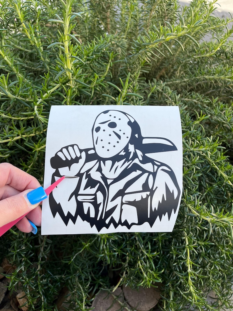 Op de afbeelding: Zwart-witte vinyl sticker van een personage met een hockeymasker dat een machete vasthoudt. Het personage draagt een jas en heeft een dreigende uitdrukking.