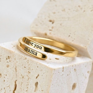 May include: A gold-toned metal wrap ring featuring an open design with two overlapping ends. The text "I love you" is engraved on the upper band, while the word "mama" is engraved on the lower band in a clear, dark, sans-serif font.