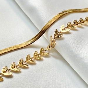 May include: A gold chain necklace featuring a delicate, leaf-shaped design. The chain is crafted in a snake-like pattern.