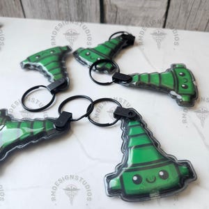 May include: Several green and black keychains with a cartoon design are displayed. Each keychain features a black keyring and a plastic charm with a smiling face. The charms have a green and black color scheme.
