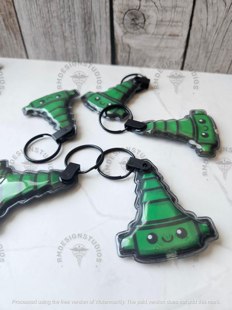 May include: Several green and black keychains with a cartoon design are displayed. Each keychain features a black keyring and a plastic charm with a smiling face. The charms have a green and black color scheme.