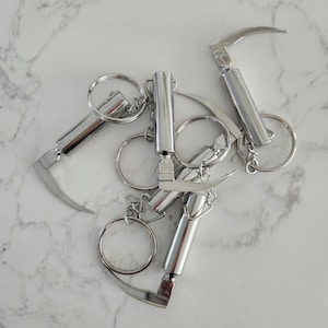 May include: A set of five silver keychains, each featuring a small, detailed sickle-shaped blade. The keychains are connected by a series of silver rings.