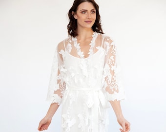 May include: White lace robe with a satin sash and floral embroidery. The robe is sheer and has a relaxed fit.