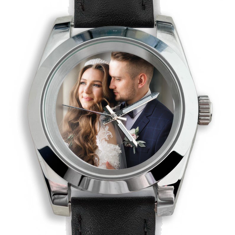 May include: Silver-toned wristwatch with a black leather band. The watch face displays a color photograph of a couple. The watch has a round face with silver hands and a silver bezel. The watch is a wedding or anniversary gift.