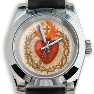 May include: A silver-toned wristwatch with a black leather band. The watch face features a religious design with a red heart, a crown of thorns, a cross, and flames. The watch hands are silver.