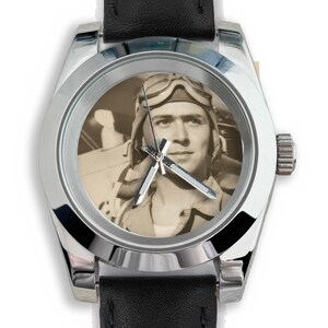 May include: Silver-toned wristwatch with a black leather band. The watch face features a sepia-toned image of a man in a pilot's cap and goggles. The watch has silver hands and a silver bezel.