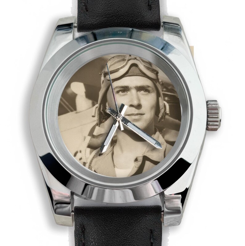 May include: Silver-toned wristwatch with a black leather band. The watch face features a sepia-toned image of a man in a pilot's cap and goggles. The watch has silver hands and a silver bezel.
