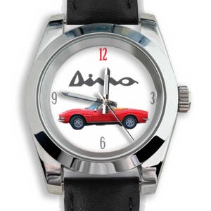May include: A wristwatch with a white face featuring a red convertible car and the word "Ainho" in black. The watch has a silver-colored bezel, black leather band, and displays the numbers 3, 6, 9, and 12.