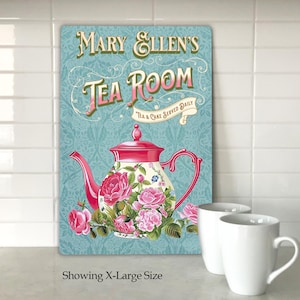 May include: A teal blue sign with white lettering that reads "Mary Ellen's Tea Room" with a pink and white teapot with floral designs and the text "Tea & Cake Served Daily".