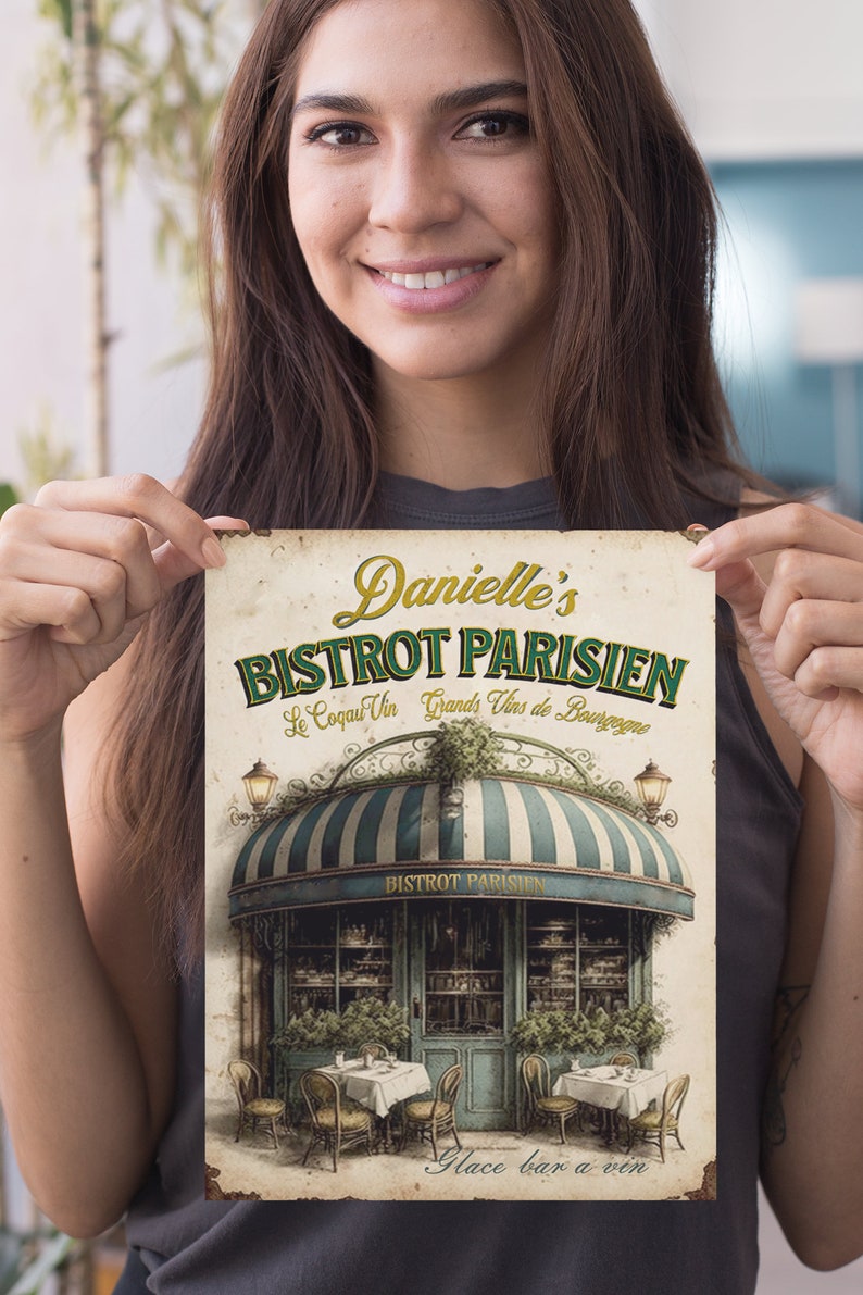 Może przedstawiać: W stylu vintage znak dla francuskiego bistro o nazwie "Danielle's Bistrot Parisien." Znak zawiera zielony daszek w białe pasy i przedstawia paryski sklep z stolikami i krzesłami na zewnątrz. Tekst "Le Coq au Vin Grands Vins de Bourgogne" jest napisany ozdobną czcionką pod nazwą bistro. Znak zawiera r&oacute;wnież tekst "Glace bar a vin" na dole.