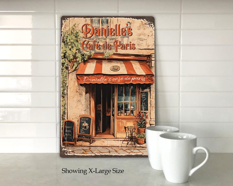 Puede incluir: Un letrero de metal de estilo vintage que representa un caf&eacute; parisino con una marquesina roja y el texto "Danielle's Cafe de Paris". El letrero tiene un aspecto desgastado y presenta un edificio de ladrillo con una puerta y ventanas.